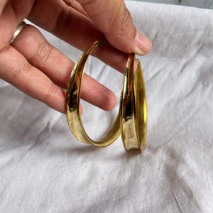 May include: A pair of gold hoop earrings with a unique curved design. The earrings are thick and have a smooth, polished finish.