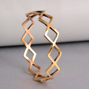 Può includere: Un braccialetto rigido in metallo dorato con un motivo geometrico a forma di diamante.
