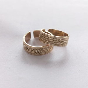Puede incluir: Dos anillos de metal dorado con un diseño trenzado. Los anillos están apilados uno encima del otro.