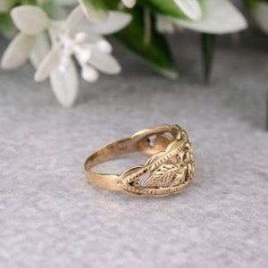 May include: A gold ring with a delicate, intricate design featuring leaves and swirls. The ring is made of a smooth, polished metal and has a classic, elegant style.