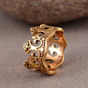 Puede incluir: Un anillo dorado con un elaborado diseño calado. El anillo presenta un estilo vintage con motivos florales y de volutas. Los intrincados detalles y los espacios abiertos le dan al anillo una apariencia delicada pero audaz. Una joya única.