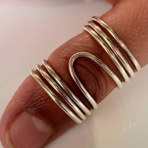 May include: A silver ring with a unique, abstract design. The ring is made of multiple bands of silver that are twisted and intertwined to create a modern and stylish look.