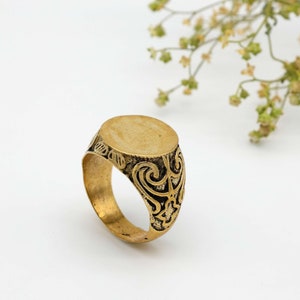 May include: A gold signet ring with an ornate design around the band and a smooth, circular top.