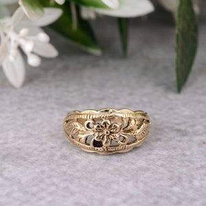May include: A gold-toned ring with a delicate floral design. The ring features a central flower with leaves on either side.
