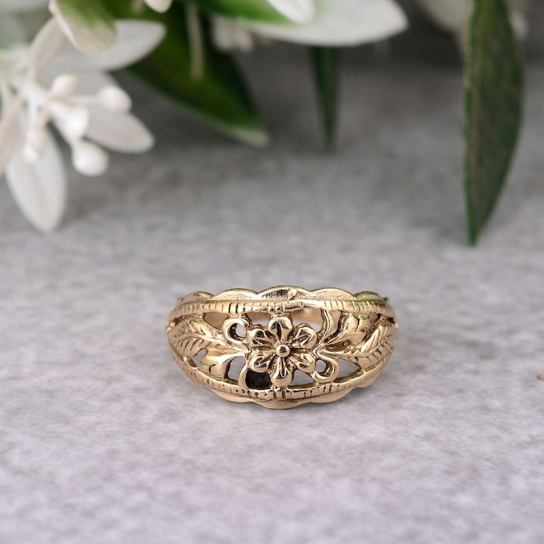 May include: A gold-toned ring with a delicate floral design. The ring features a central flower with leaves on either side.