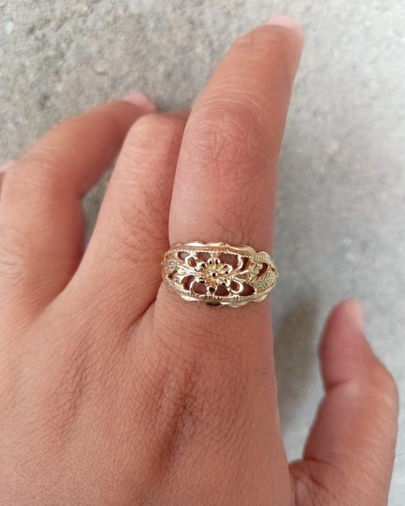 May include: A gold ring with a delicate floral design. The ring is worn on a finger.