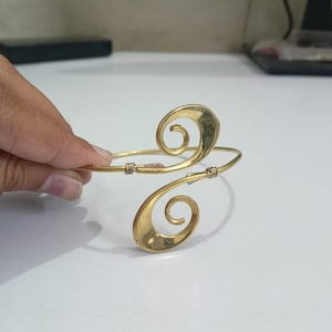 Pu&ograve; includere: Un braccialetto in metallo dorato con un design unico a doppia spirale. Il braccialetto &egrave; aperto e regolabile.