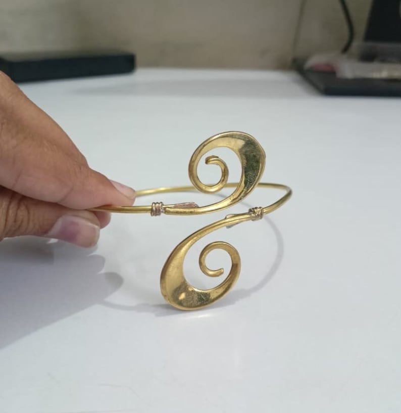 Pu&ograve; includere: Un braccialetto in metallo dorato con un design unico a doppia spirale. Il braccialetto &egrave; aperto e regolabile.