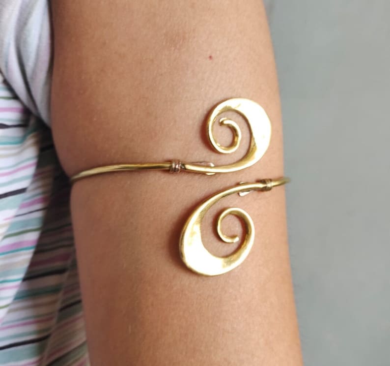 Pu&ograve; includere: Un braccialetto per braccio in metallo dorato con un design a doppia spirale. Il braccialetto &egrave; aperto e regolabile.