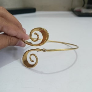 Pu&ograve; includere: Un braccialetto in metallo dorato con un design unico che presenta due forme a spirale. Il braccialetto &egrave; aperto e regolabile.