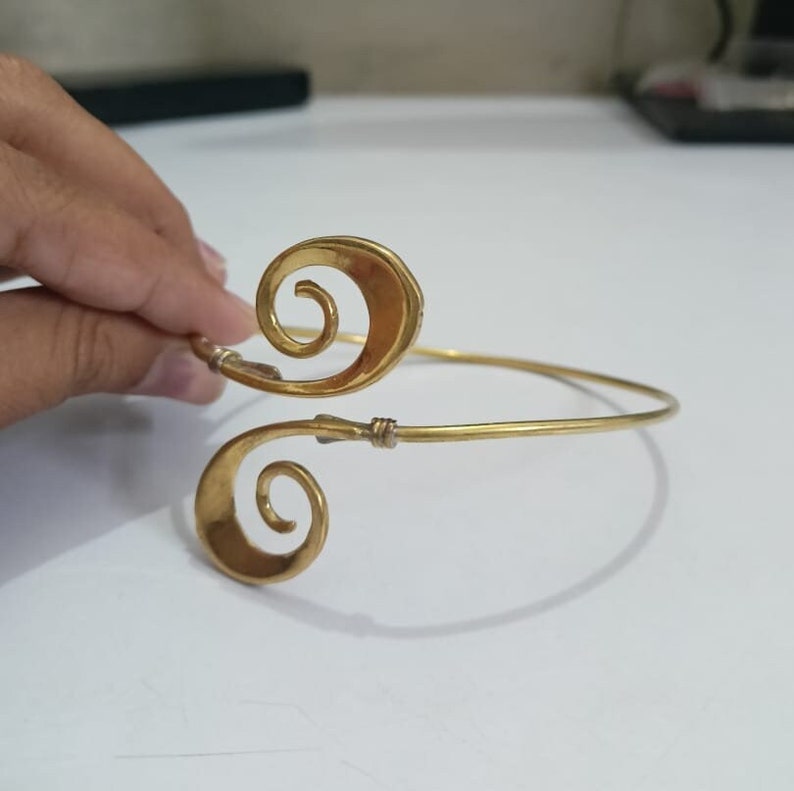 Pu&ograve; includere: Un braccialetto in metallo dorato con un design unico che presenta due forme a spirale. Il braccialetto &egrave; aperto e regolabile.