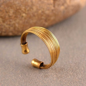 May include: A gold-toned adjustable ring made of multiple thin wires woven together. The ring is open ended and has a smooth, polished finish.