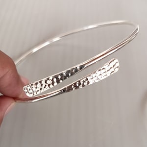 Op de afbeelding: Een zilveren armband met een gehamerde textuur. De armband is open en heeft een eenvoudig ontwerp.