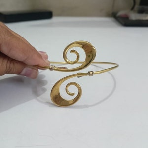 Pu&ograve; includere: Un braccialetto in metallo dorato con un design a doppia spirale. Il braccialetto &egrave; aperto e regolabile.