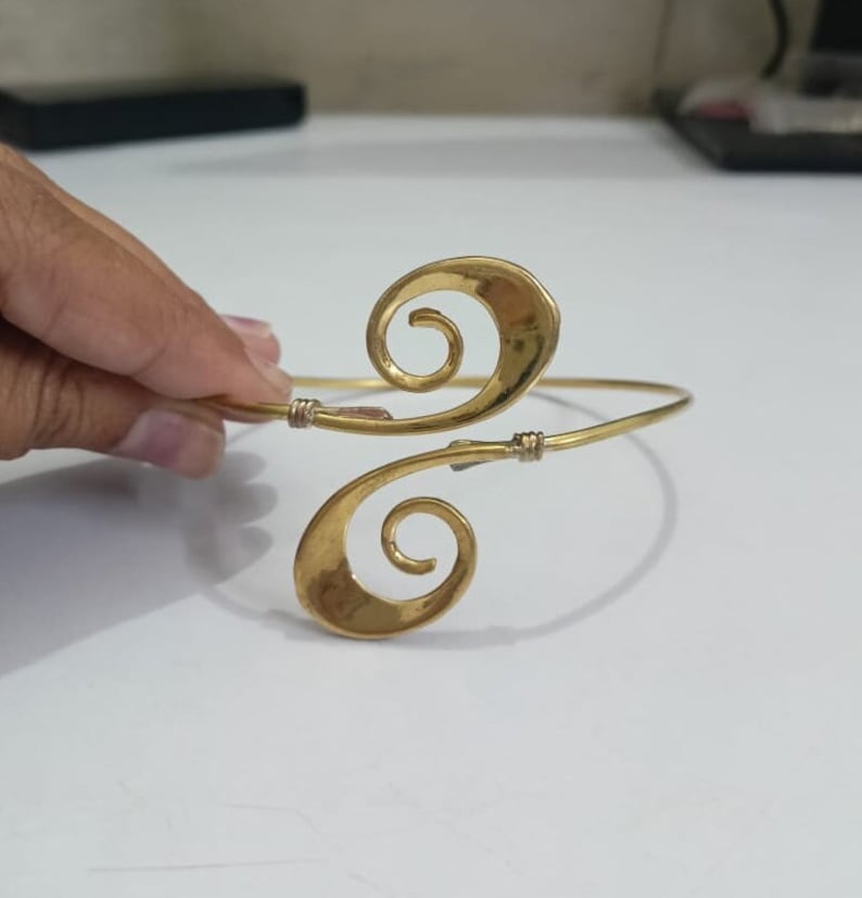Pu&ograve; includere: Un braccialetto in metallo dorato con un design a doppia spirale. Il braccialetto &egrave; aperto e regolabile.