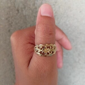 May include: A gold filigree ring with a floral design. The ring is worn on a person's thumb.
