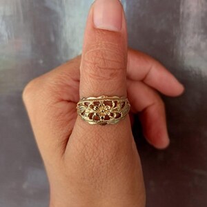 May include: A gold filigree ring with a floral design. The ring is worn on a person's thumb.