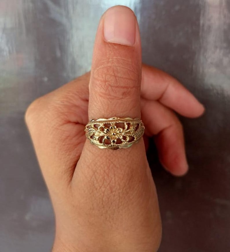 May include: A gold filigree ring with a floral design. The ring is worn on a person's thumb.
