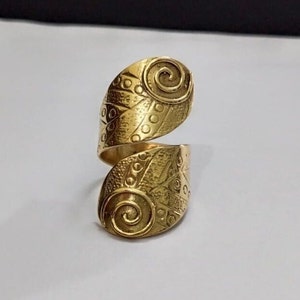 May include: A gold-toned adjustable ring with a spiral and geometric design. The ring is made of metal and has a textured finish.