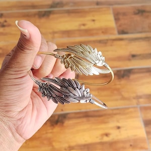 May include: Two silver and gold leaf-shaped bangles. The bangles are open and have a delicate design.