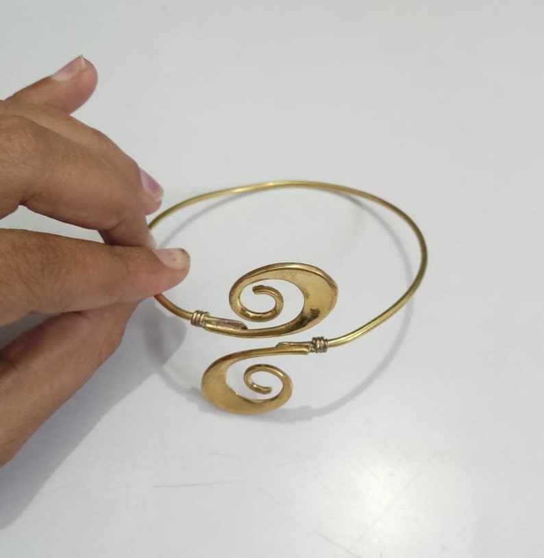Pu&ograve; includere: Un braccialetto in metallo dorato con un design unico che presenta due forme a spirale. Il braccialetto &egrave; aperto e regolabile.