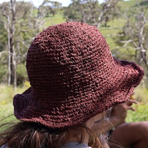 May include: A person wearing a brown crocheted sun hat with a wide brim. The hat is made of a textured material and has a simple design.