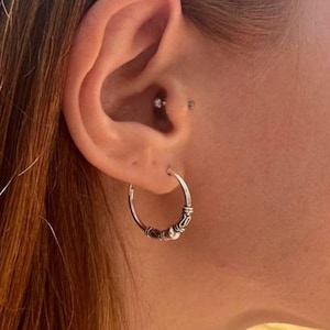 May include: A close-up of a person's ear wearing a silver hoop earring. The earring has a decorative design with small beads and a textured pattern. The person has long, reddish-brown hair.
