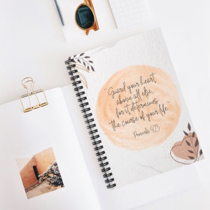 May include: A spiral bound notebook with a watercolor background and the quote "Guard your heart above all else, for it determines the course of your life." Proverbs 4:23