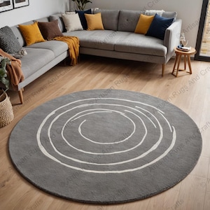 Puede incluir: Una alfombra redonda gris con un patrón de espiral blanco. La alfombra está en una sala de estar con un sofá seccional gris y una mesa auxiliar de madera.