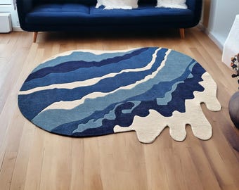 May include: An abstract rug with a unique shape and a color palette of blues and off-white. The rug features a layered design, resembling waves or a topographical map. It is placed on a hardwood floor, adding a touch of modern art to the room.