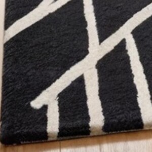 May include: Black and white geometric patterned rug with a fuzzy texture. The rug has a modern design with white lines on a black background.