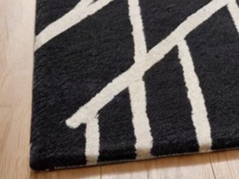 May include: Black and white geometric patterned rug with a fuzzy texture. The rug has a modern design with white lines on a black background.