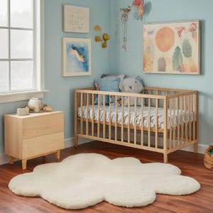 Op de afbeelding: Een wit wolkenvormig tapijt in een kinderkamer met een houten wieg, een lichtblauwe muur en kunstwerken aan de muur.