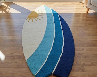 May include: A surfboard-shaped rug with a sun design. The rug has a white background with a yellow sun in the upper left corner. Blue stripes of varying shades run down the length of the rug, separated by white stripes.