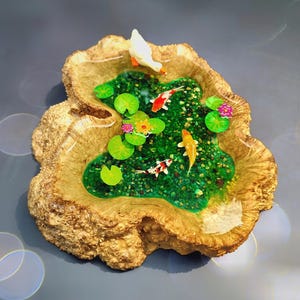 May include: A miniature resin pond with a wooden base, featuring a white bird, green lily pads, and orange and white koi fish.