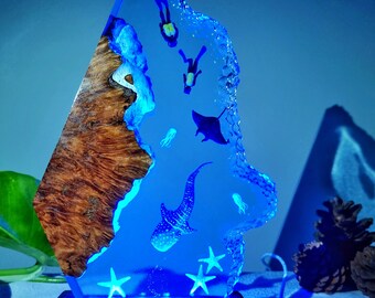 May include: A blue resin sculpture of a whale shark, manta ray, and divers, set in a wooden base with a blue LED light. The sculpture is made to look like a piece of ocean with a coral reef on one side.