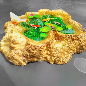 May include: A wooden base with a resin pond filled with green water, lily pads, and colorful fish. A white bird figurine is perched on the edge of the pond.