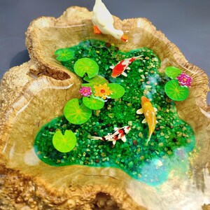 May include: A miniature resin pond scene with a white duck, green lily pads, and orange and white koi fish. The pond is set in a wooden bowl with a natural wood grain.