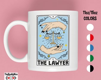 Könnte beinhalten: Weiße Keramiktasse mit einem Tarotkarten-Design mit blauem Hintergrund, zwei Händen, die eine Waage halten, und dem Text "THE LAWYER".