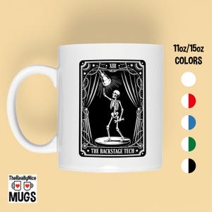 May include: White ceramic mug featuring a black and white illustration of a skeleton holding a spotlight on a stage. The text "THE BACKSTAGE TECH" is below the image. The mug also has the text "11oz/15oz COLORS".