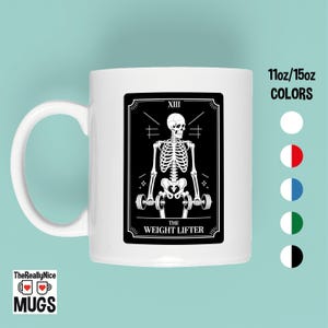 Puede incluir: Taza de cerámica blanca con una ilustración en blanco y negro de un esqueleto levantando pesas, con la leyenda "The Weight Lifter". La taza también tiene el texto "11oz/15oz COLORS" y el logo "TheReallyNice MUGS".