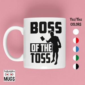 May include: White ceramic mug with a black silhouette of a person throwing a bag of chips. The text "Boss of the Toss" is printed in black on the mug. The mug is available in 11oz or 15oz sizes and in a variety of colors.