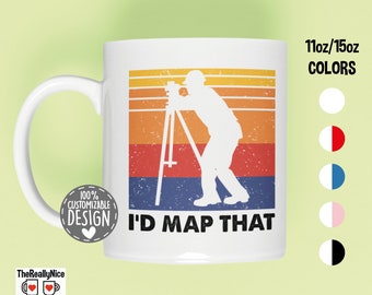 Könnte beinhalten: Eine weiße Keramiktasse mit einem Retro-Design, das die Silhouette eines Vermessers zeigt, der ein Theodolit hält. Der Text "I'd Map That" ist in Schwarz unter dem Bild gedruckt. Die Tasse ist in 11oz oder 15oz und in verschiedenen Farben erhältlich.