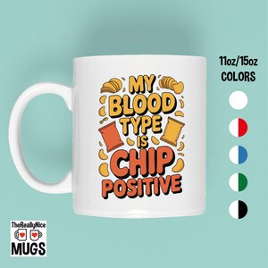 May include: White ceramic mug with the text "MY BLOOD TYPE IS CHIP POSITIVE" in orange and yellow. The mug features illustrations of chips and chip bags. The mug is available in 11oz and 15oz sizes.
