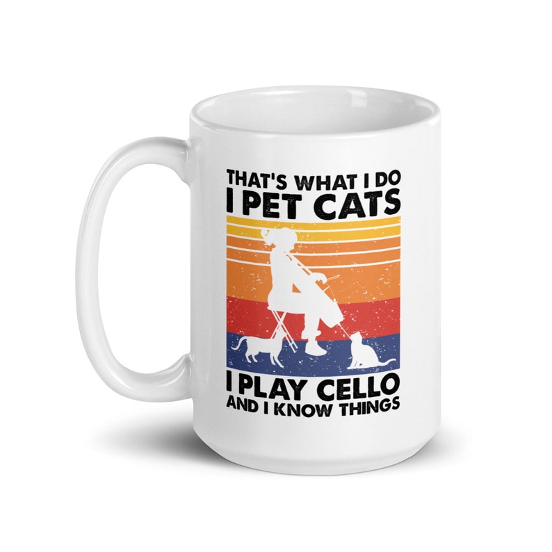 May include: White ceramic mug with a black and white illustration of a person playing the cello with two cats. The text on the mug reads "That's what I do I pet cats I play cello and I know things".