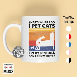 May include: White ceramic mug with a retro design featuring a person playing pinball and a cat. The text reads "That's what I do I pet cats I play pinball and I know things".