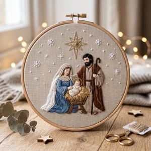 May include: A circular wooden embroidery hoop featuring a hand-stitched nativity scene on beige fabric. The design depicts a figure in a blue robe, a figure in a brown robe with a staff, and an infant in a manger, all beneath a gold star.