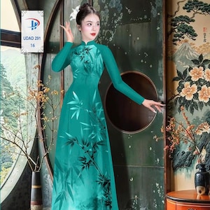 May include: A teal-colored, long-sleeved dress with a mandarin collar and a flowing silhouette. The dress features a bamboo leaf design in black. The image also includes a small white tag with the text "UDAD 291 16".