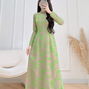 May include: A full-length dress with long sleeves and a high collar. The dress has a pattern of green brushstrokes on a pinkish-beige base. The sleeves are sheer, and the fabric looks lightweight. The dress has an elegant, flowing style.