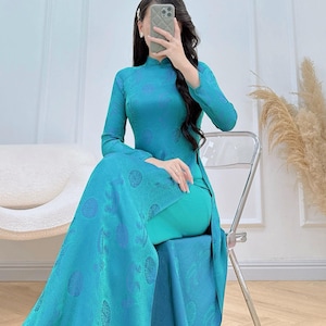 Könnte beinhalten: Türkisfarbenes, langärmliges Kleid mit hohem Ausschnitt und fließendem Rock. Das Kleid hat ein dezentes Muster und wird mit einer passenden türkisfarbenen Hose getragen. Geeignet für formelle Anlässe.